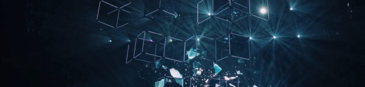 A digital art piece features glowing 3D wireframe cubes suspended in a dark space. Bright beams of light and ethereal particles surround the cubes, creating a futuristic and abstract atmosphere.