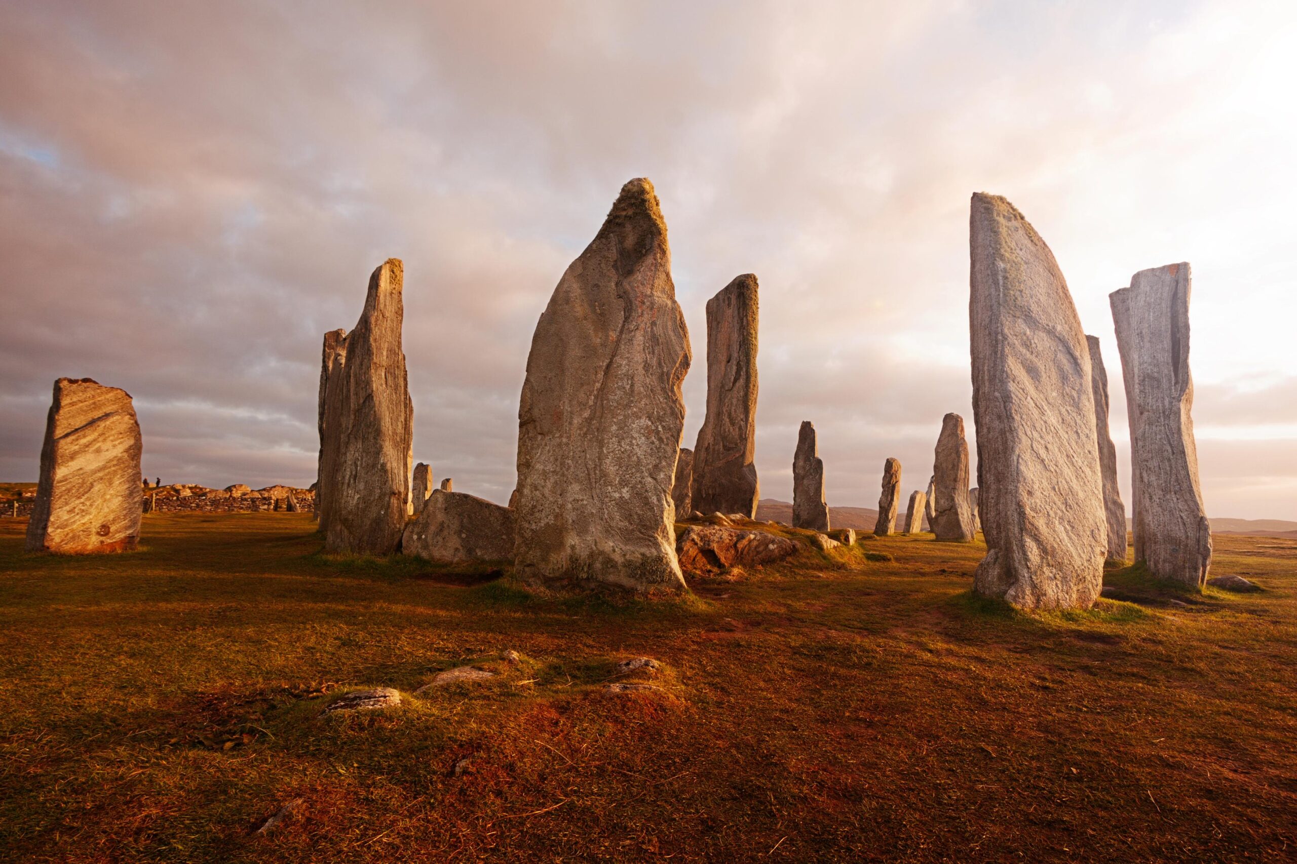 Large, weathered standing stones form a circle on grassy, sunlit ground under a cloudy sky, creating an ancient and mysterious atmosphere reminiscent of sites studied in BA Hons History London courses.