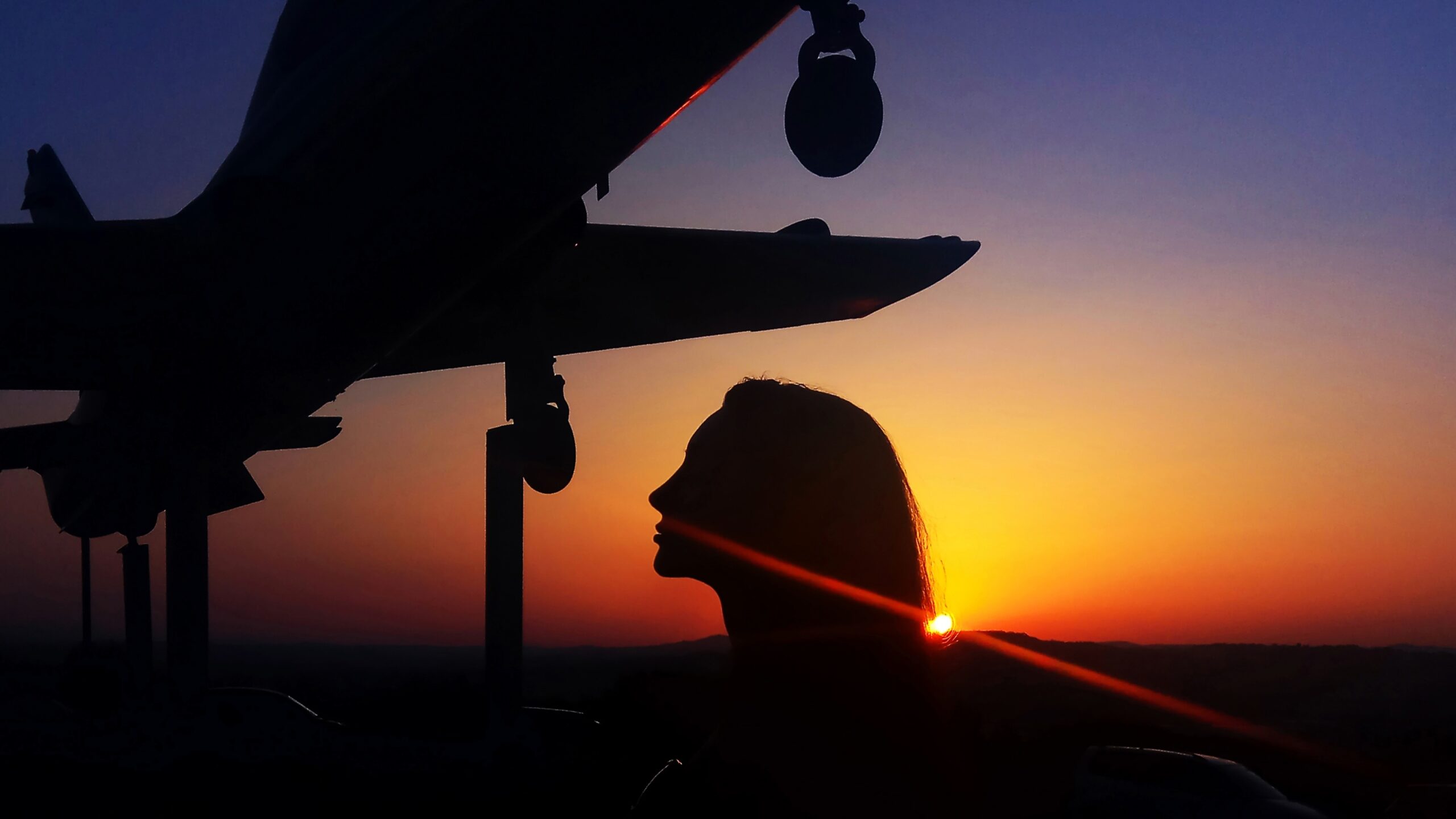 A silhouette of a person in profile stands beneath an airplane on stilts at sunset, the sky glowing with orange and purple hues—an inspiring scene for anyone studying BSc (Hons) Politics & International Relations London.