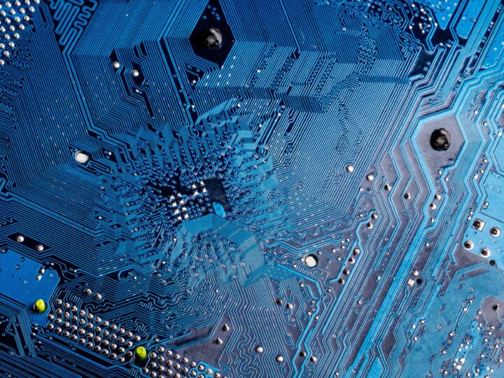 Close-up of a blue printed circuit board with intricate electronic pathways, small metallic components, and a few screws—reflecting the precision and complexity found in Philosophy & Computer Science BSc (Hons) London studies.