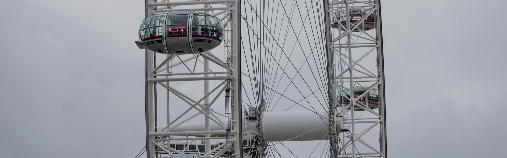 Close-up view of a large Ferris wheel with several glass-enclosed capsules against a cloudy sky. The metal framework is visible, showcasing the intricate design of the structure.
