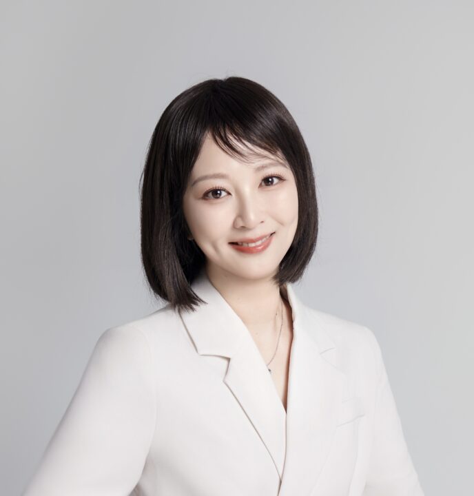 Chunyan Wu, a woman with straight dark hair and light skin, smiles at the camera. She is wearing a white blazer over a light top and a simple necklace, set against a plain light gray background.