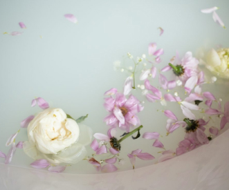 A soothing bath with milky water, adorned with white and pink flowers, and scattered petals floating on the surface, creating a serene and calming atmosphere.