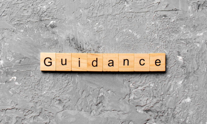 Wooden letter tiles spelling "Guidance" are arranged in a row on a textured gray surface.