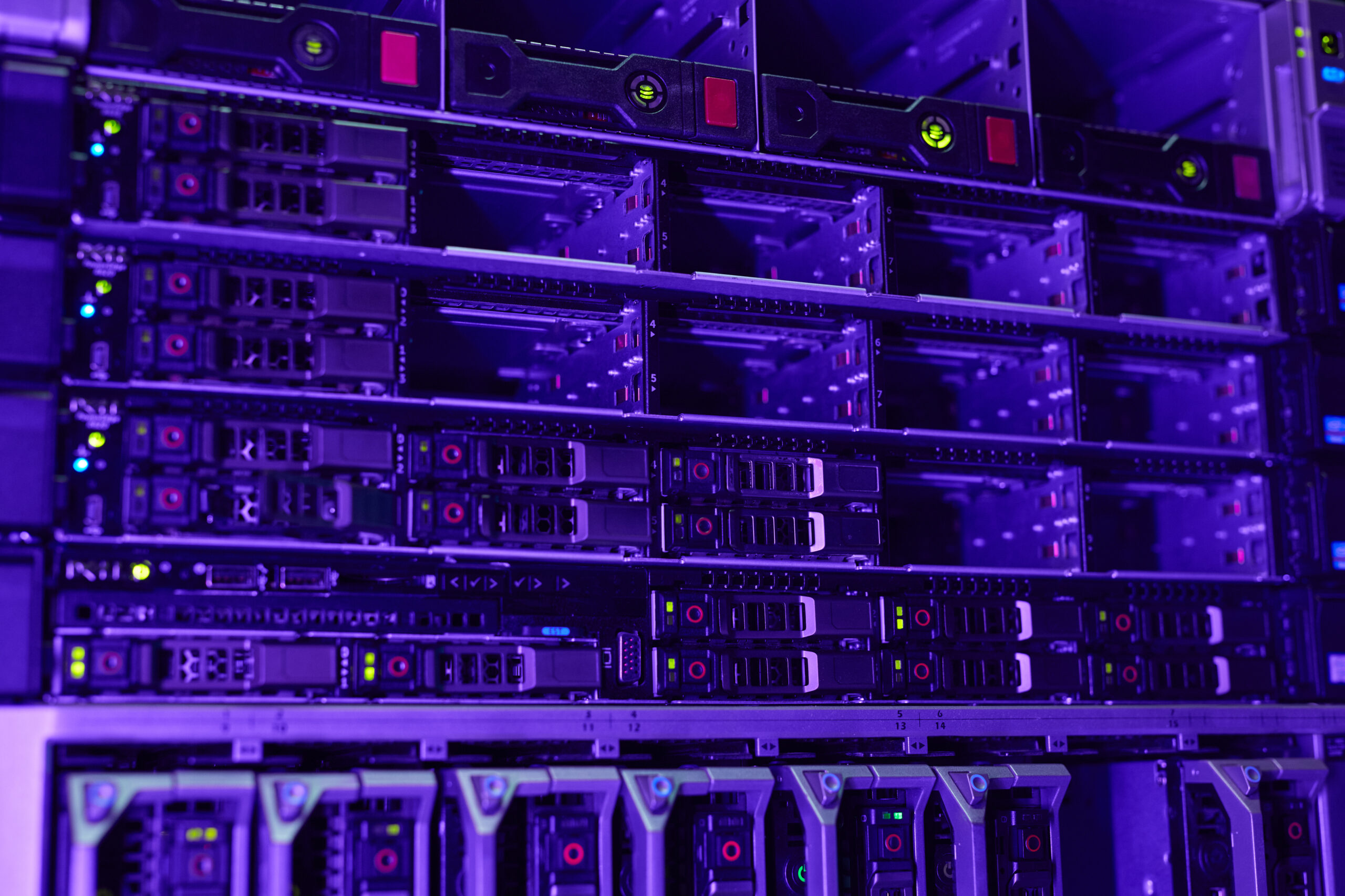 Close-up of multiple server racks with blinking lights and hardware components, illuminated by purple lighting in a data center environment supporting advanced research and PhD programmes.