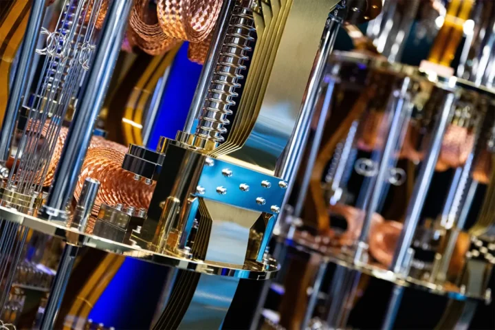 Close-up view of the intricate metallic and copper components inside a quantum computer, featuring coils, tubes, and reflective surfaces with a blue-lit background.
