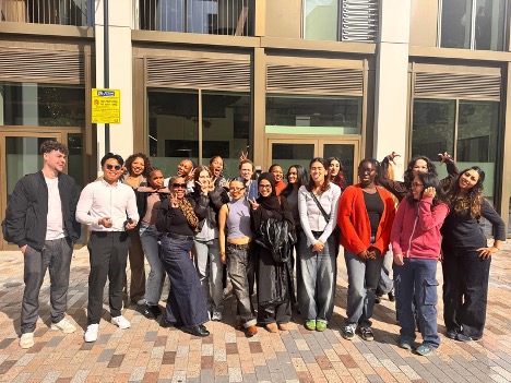 A diverse group of sixteen young adults standing together outside a modern building.
