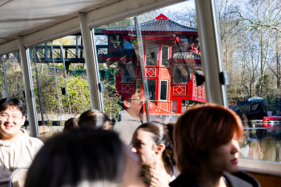 Passengers on a boat looking out at a red, Asian-style pagoda structure on the riverbank.