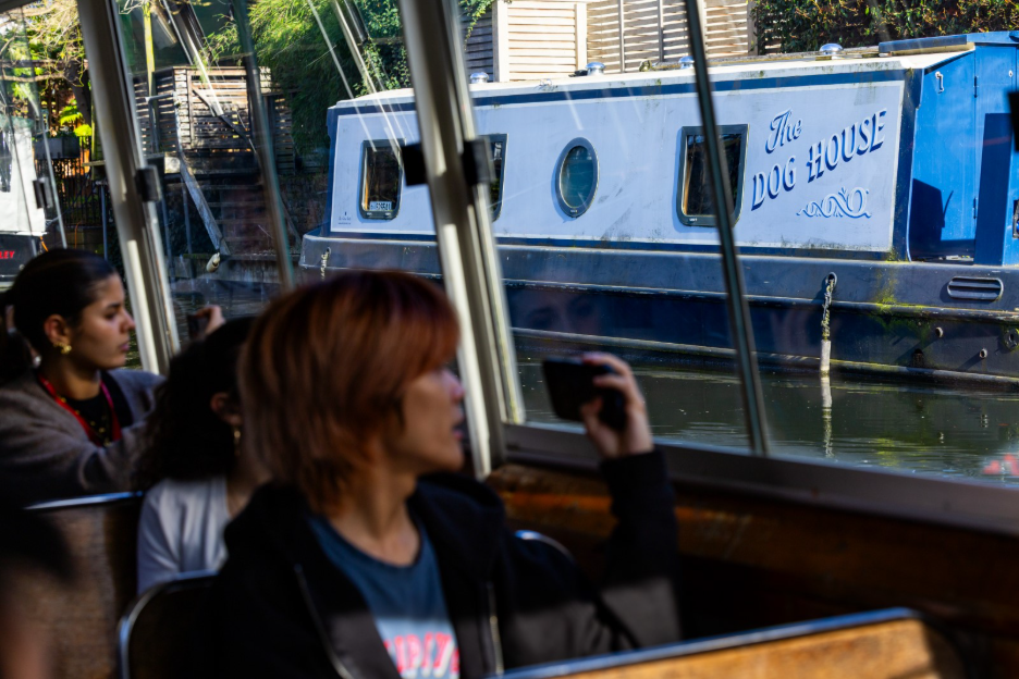 People on a boat tour look toward a canal narrowboat named “The Dog House.”